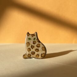 Broche en forme de chat assis en émaux sur cuivre cloisonnés. Son pelage est couleur léopard et ses yeux sont verts.