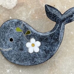 Broche en forme de baleine en émaux sur cuivre cloisonnés. La couleur de la baleine est un dégradé de gris chiné. Son œil est noir.Elle est décorée par une marguerite.