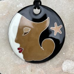 Pendentif rond en émaux sur cuivre cloisonnés qui représente une dame de profil. Elle a les yeux fermés. Ses cheveux sont noirs. Elle a une étoile dans les cheveux.