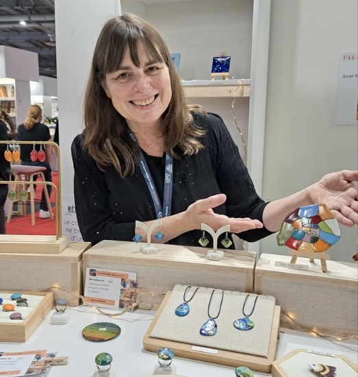 Artisane souriante montrant ses créations d'émaux sur cuivre sur le stand du salon du Made In France à Paris