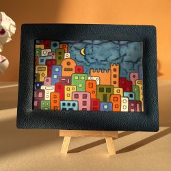 Tableau en émaux sur cuivre cloisonnés représentant un village des Cinque Terre. Les cloisons délimitent chaque bâtiment qui ont chacun une couleur différente. Il y a un croissant de lune dans le ciel nuageux. Le tableau est encadré de cuir bleu.